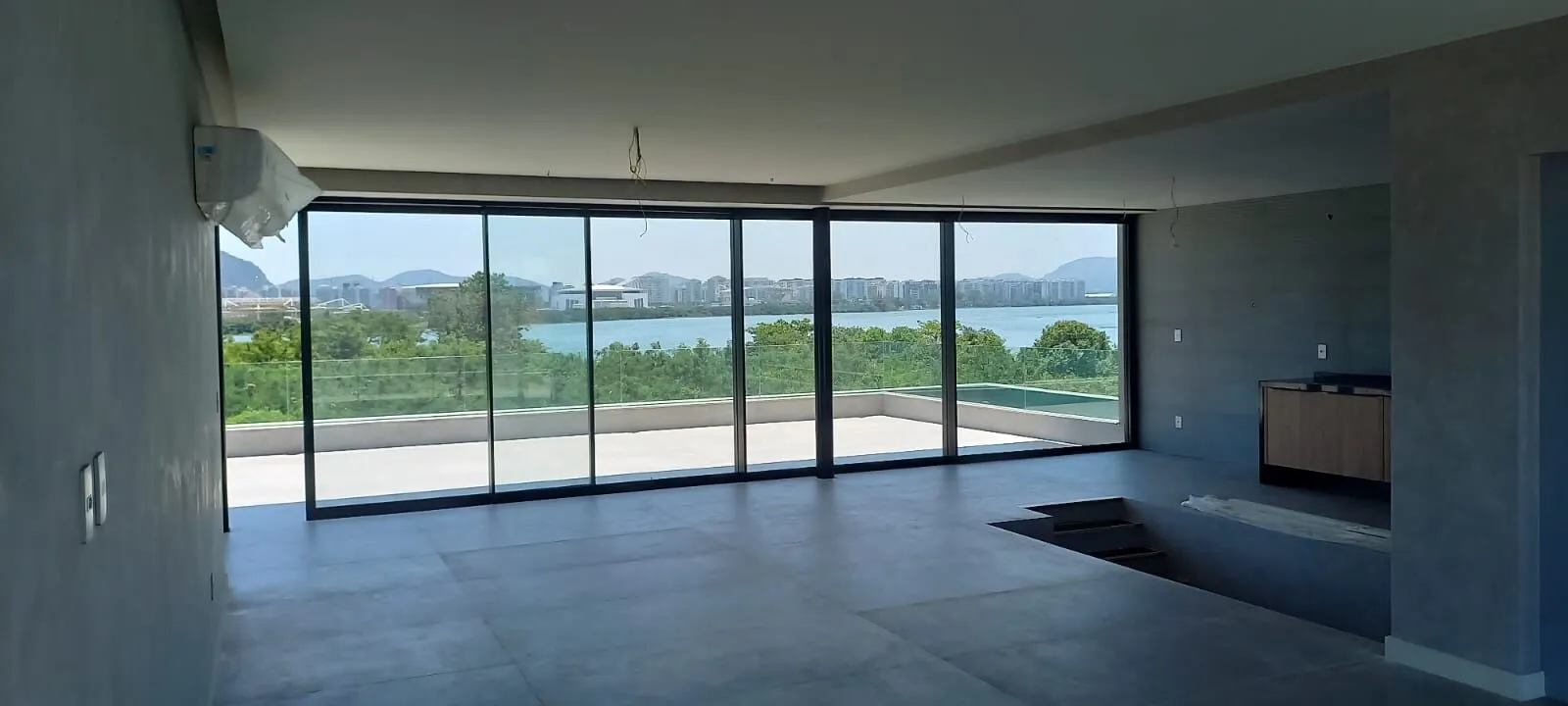 Salão panorâmico com painéis de vidro do piso ao teto e vista para a Lagoa de Marapendi na Mansão Alphaville 1200m²