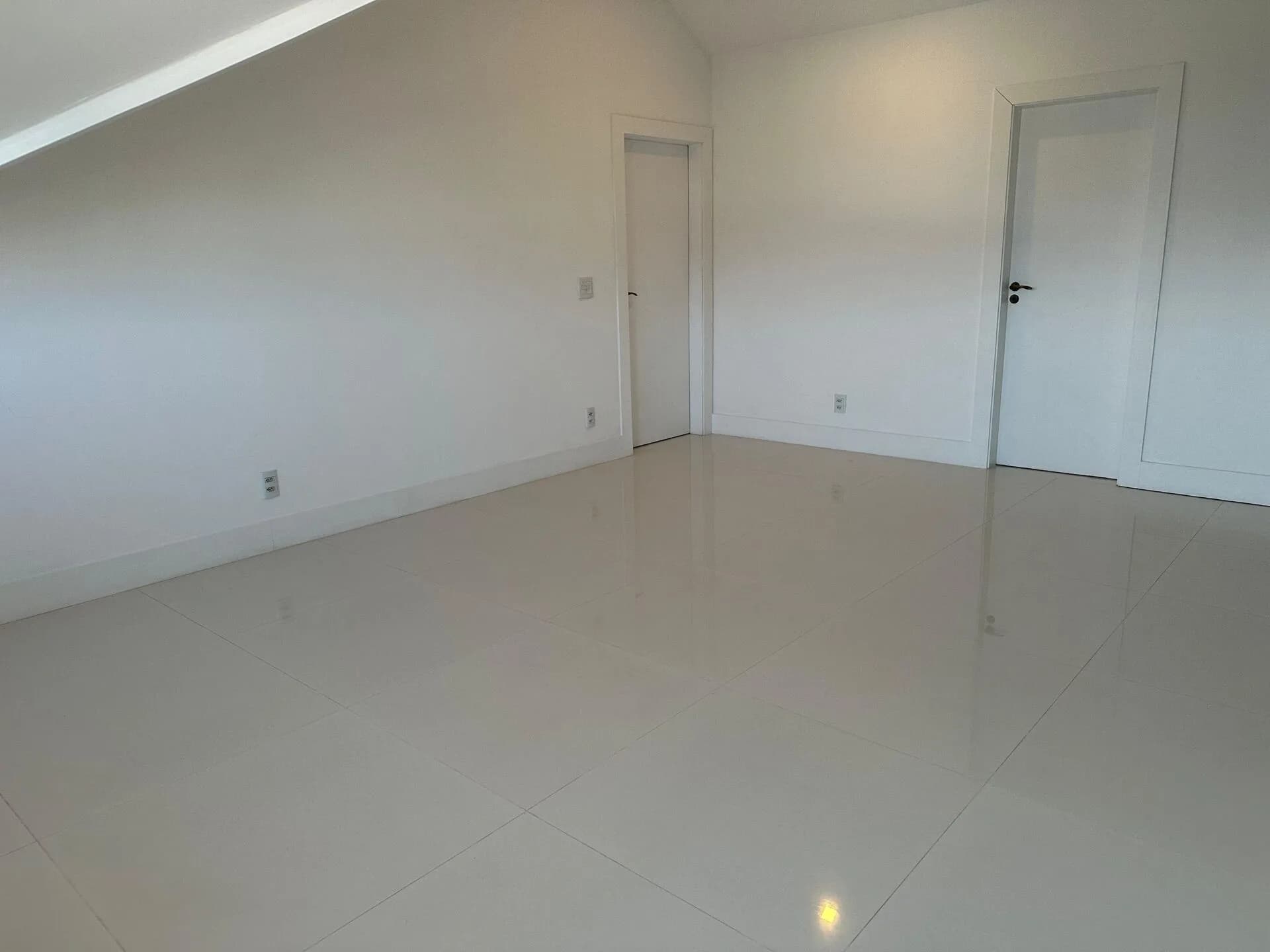 Cômodo do sótão com duas portas, teto inclinado e piso porcelanato na casa duplex 500m² no Alphaville