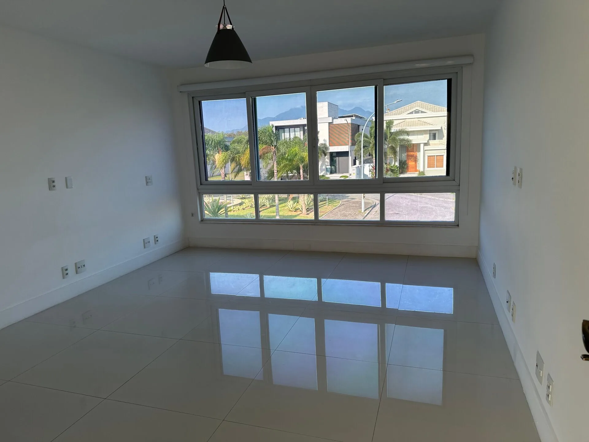 Suíte ampla com janelão panorâmico, vista para o condomínio Alphaville, piso porcelanato e luminária pendente