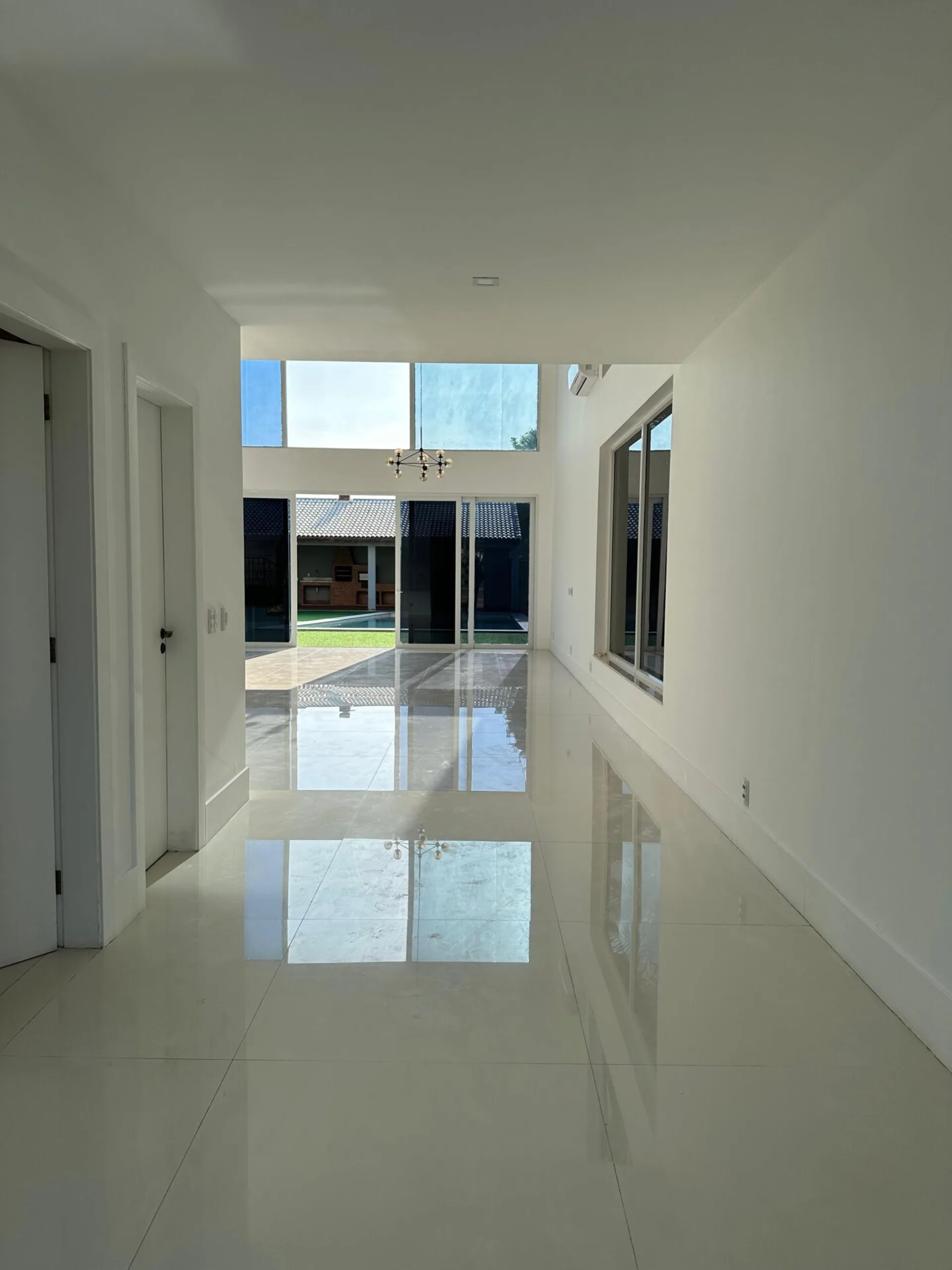 Sala com pé direito duplo, lustre moderno, portas de vidro e vista integrada para área gourmet e piscina no Alphaville