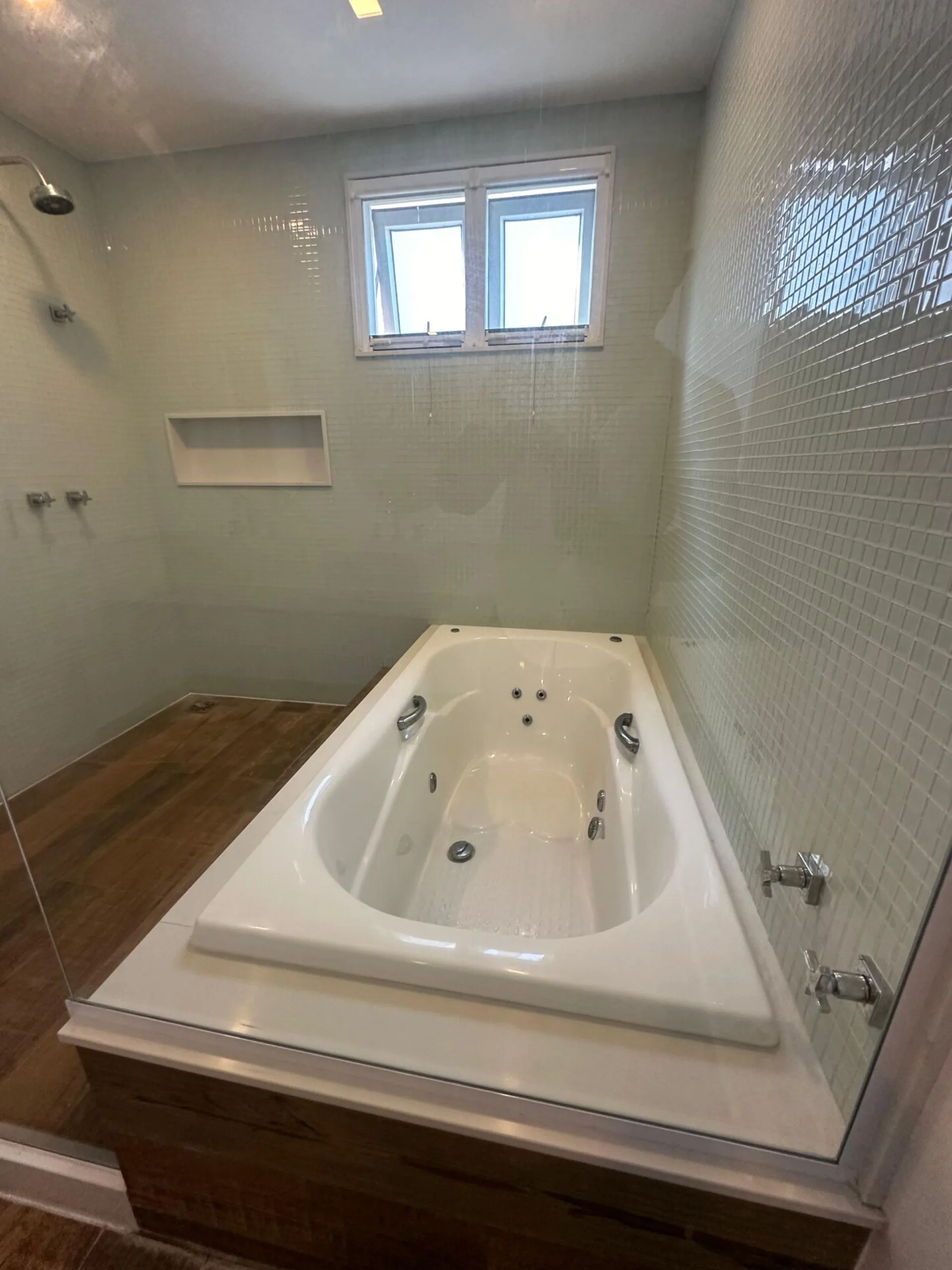 Banheira de hidromassagem com acabamento em pastilhas de vidro, piso de madeira e nicho embutido no box