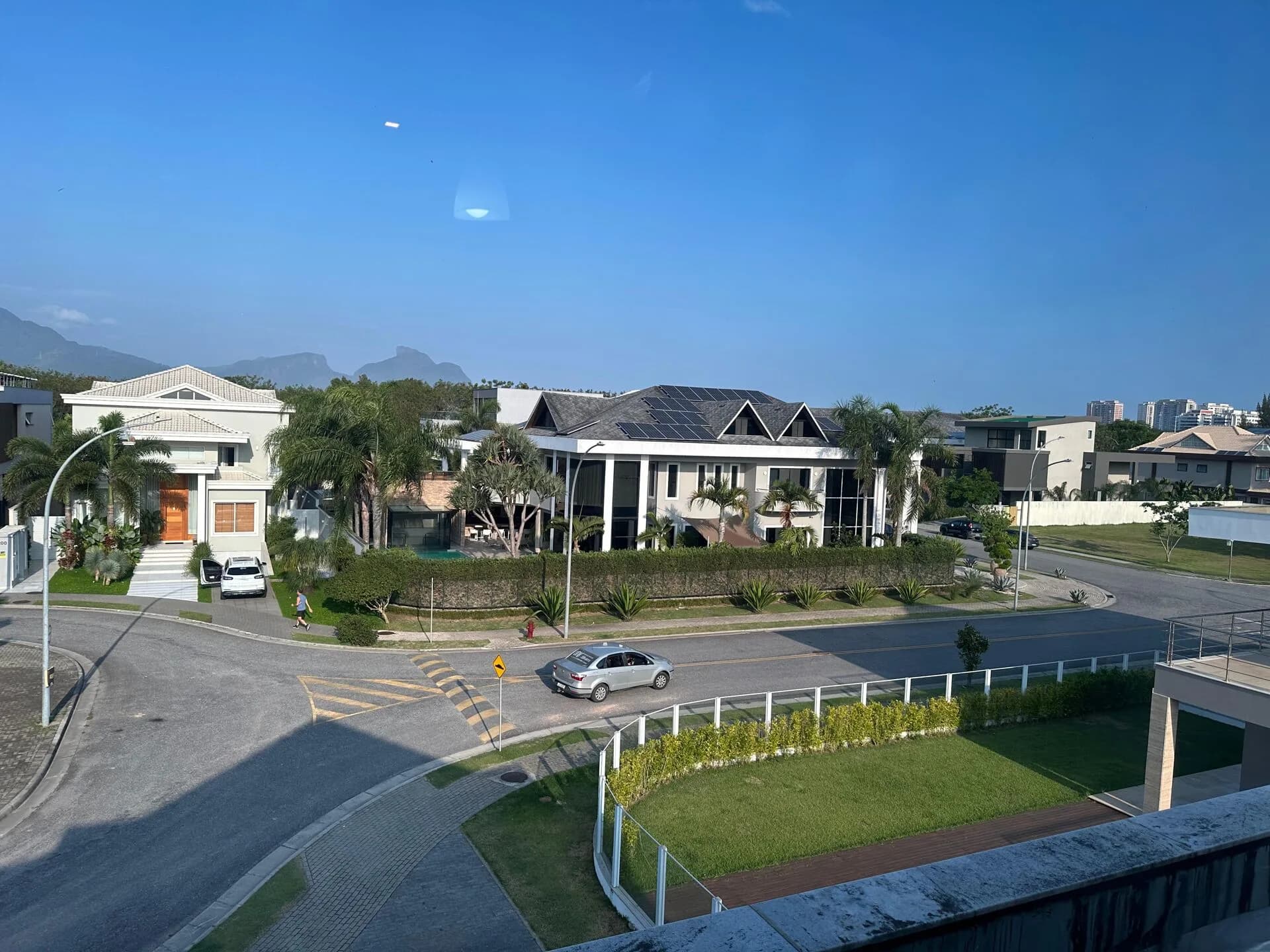 Vista aérea panorâmica do condomínio Alphaville Barra da Tijuca com casas de alto padrão, palmeiras e montanhas ao fundo