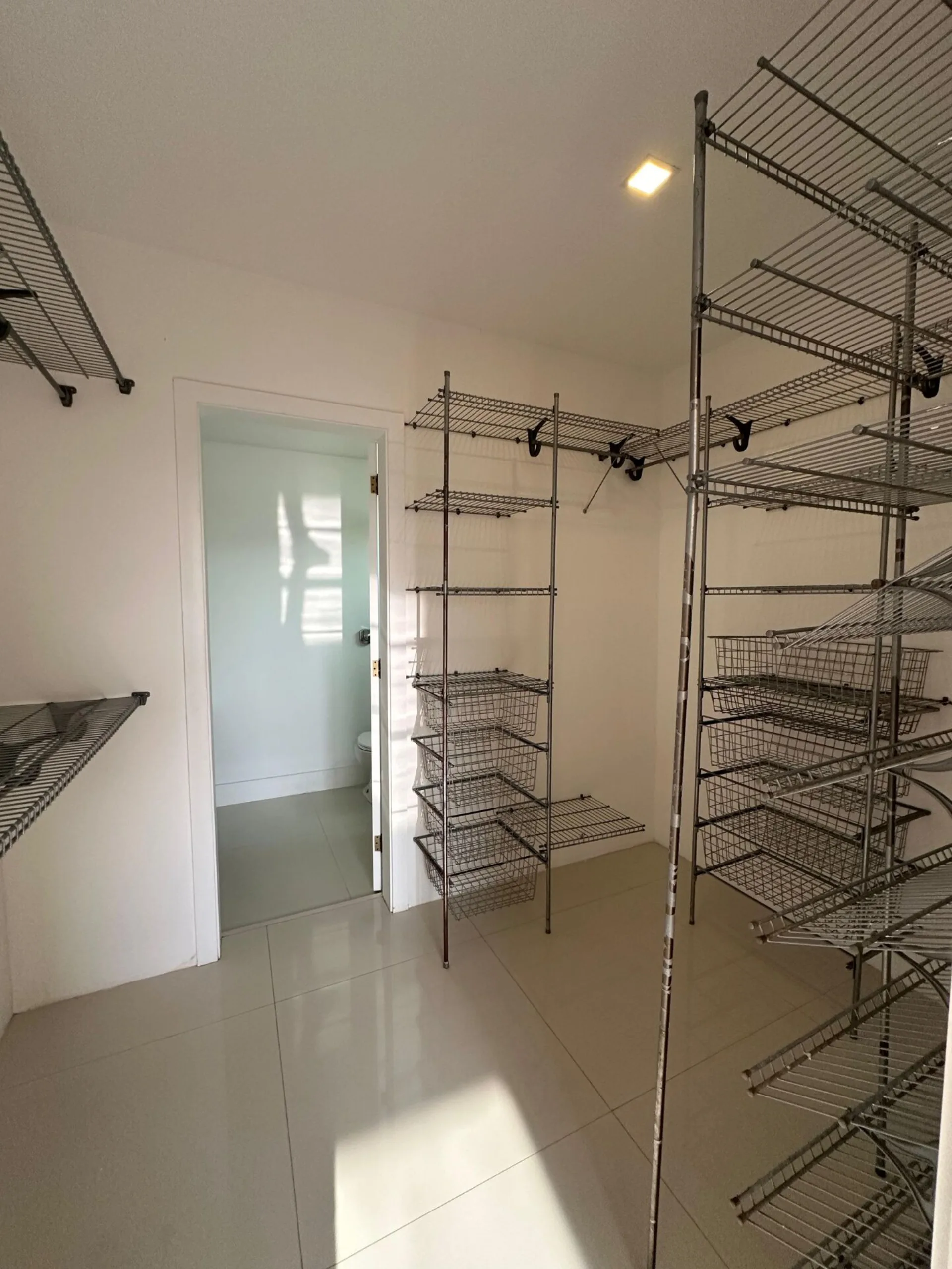 Closet da dependência com prateleiras aramadas, cestos organizadores e acesso ao banheiro na casa Alphaville 500m²