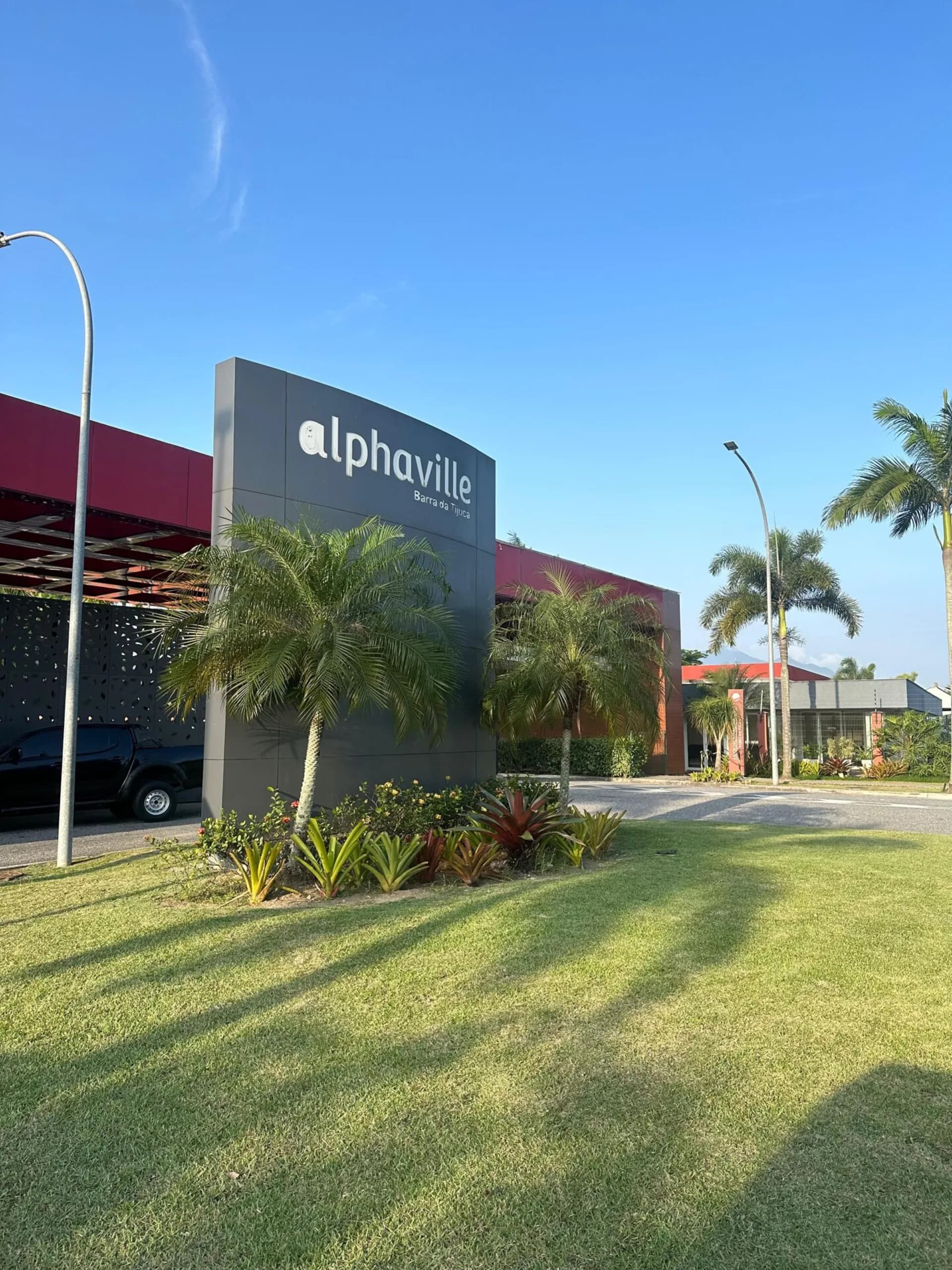Portaria e entrada principal do condomínio Alphaville Barra da Tijuca com totem de identificação, palmeiras e jardim tropical