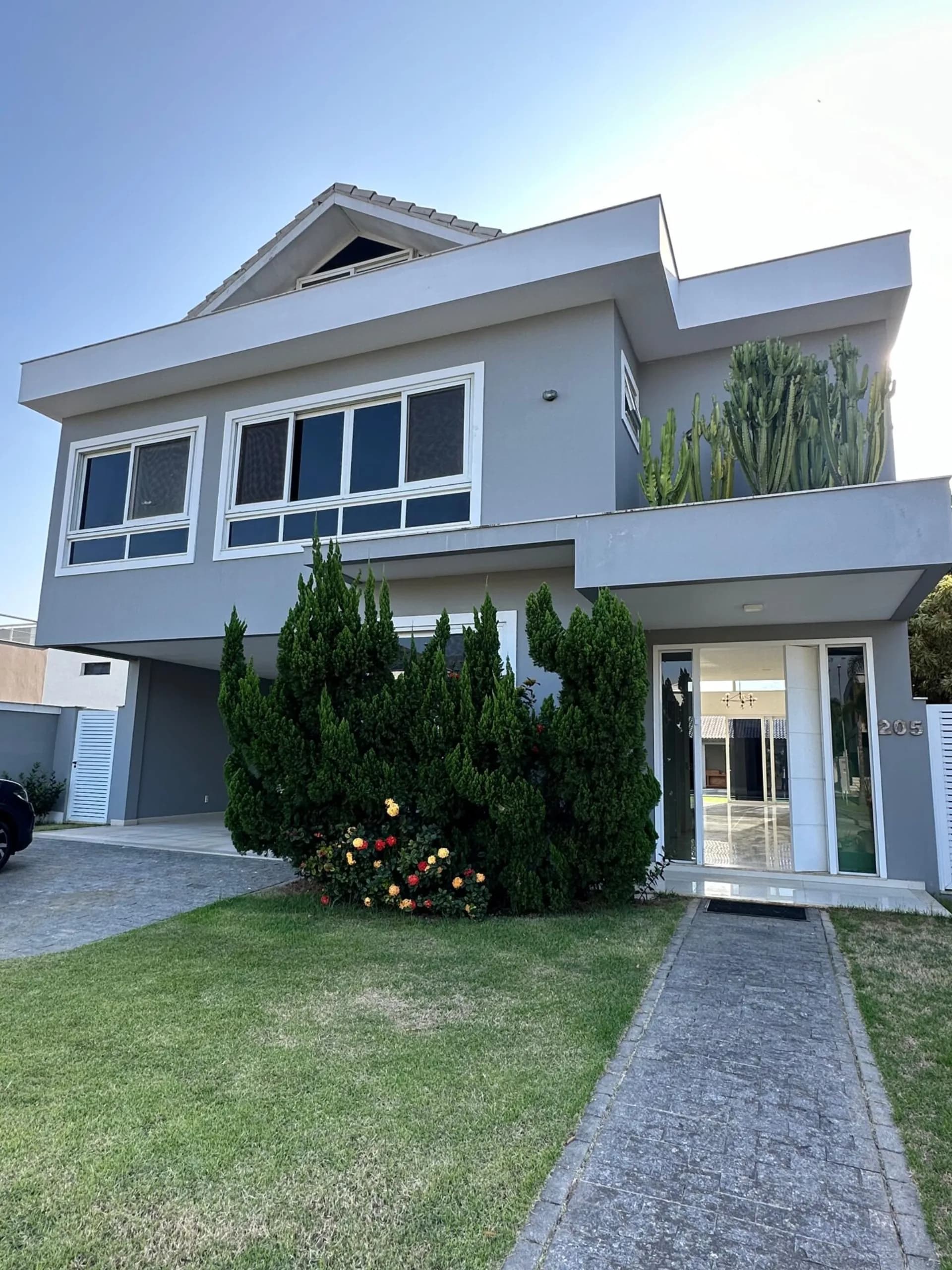 Fachada frontal da casa duplex 500m² com jardim, caminho de pedra, ciprestes e cactos no Alphaville Barra da Tijuca