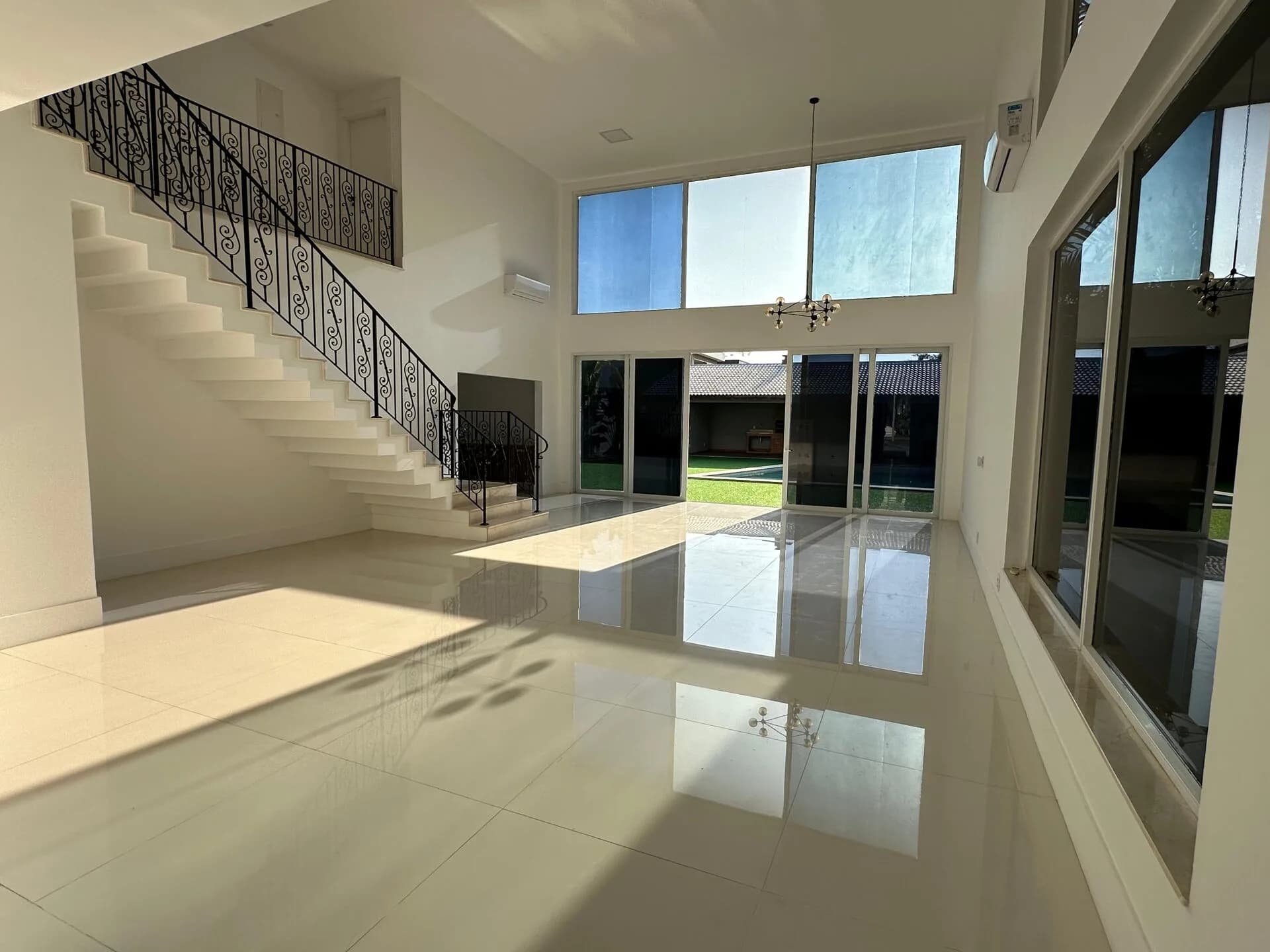 Sala ampla com pé direito duplo, piso porcelanato polido, escada com corrimão de ferro forjado e porta de correr para a piscina