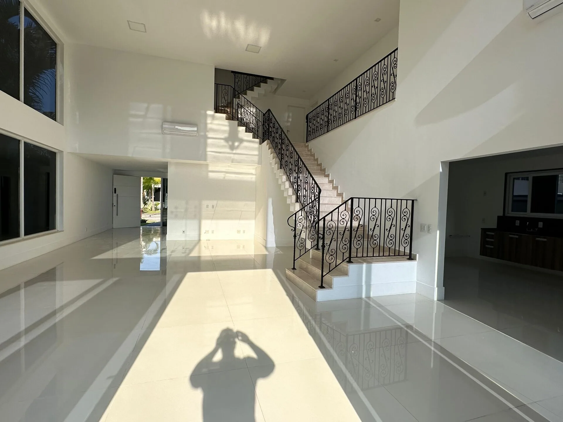 Sala em ângulo frontal com escada dupla em ferro forjado, pé direito duplo e piso porcelanato na casa Alphaville 500m²