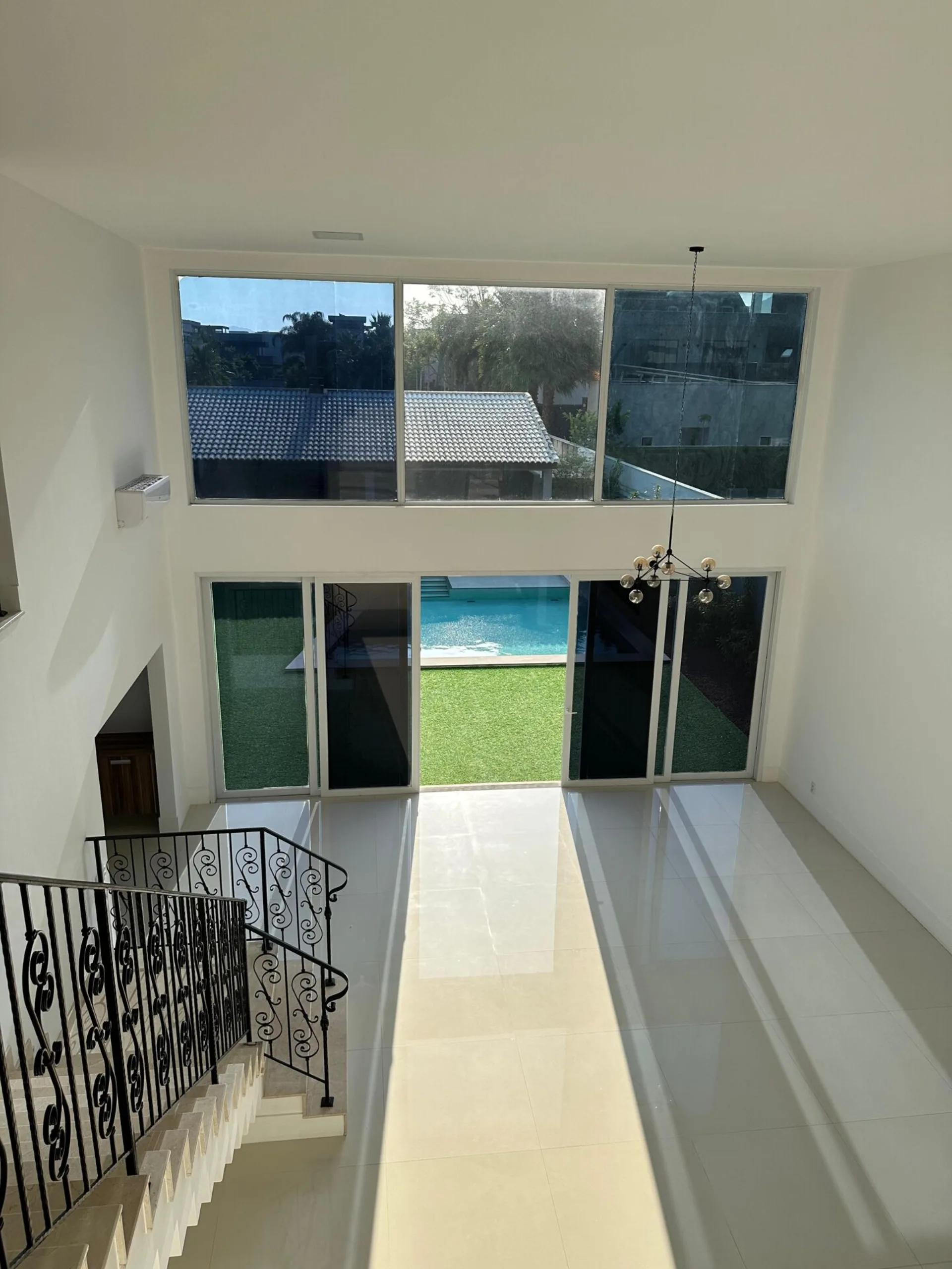 Vista do segundo andar da sala com pé direito duplo, janelões com vista para piscina e lustre moderno na casa Alphaville