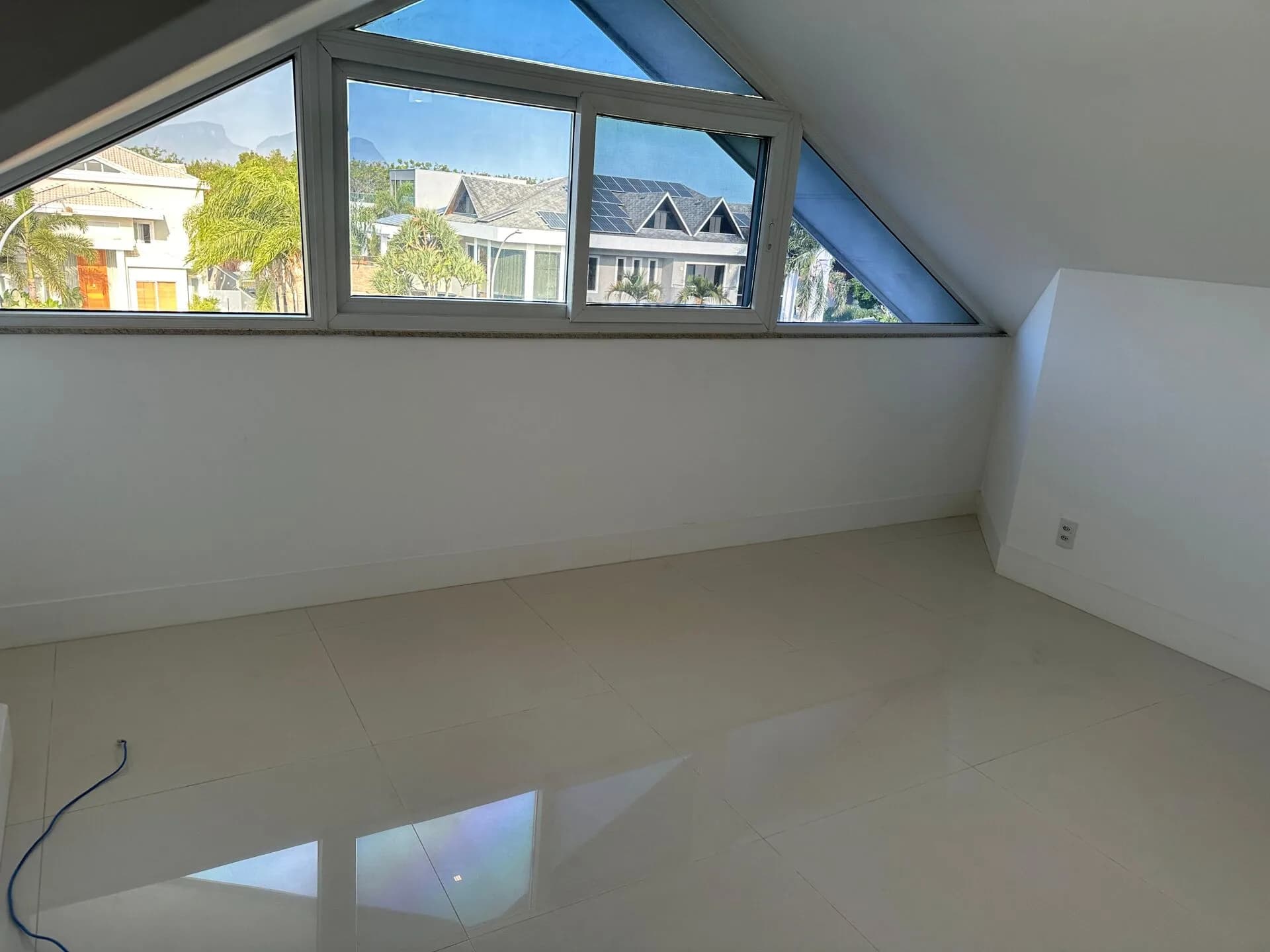 Sótão amplo com janela triangular panorâmica, piso porcelanato e vista para as casas do Alphaville Barra da Tijuca