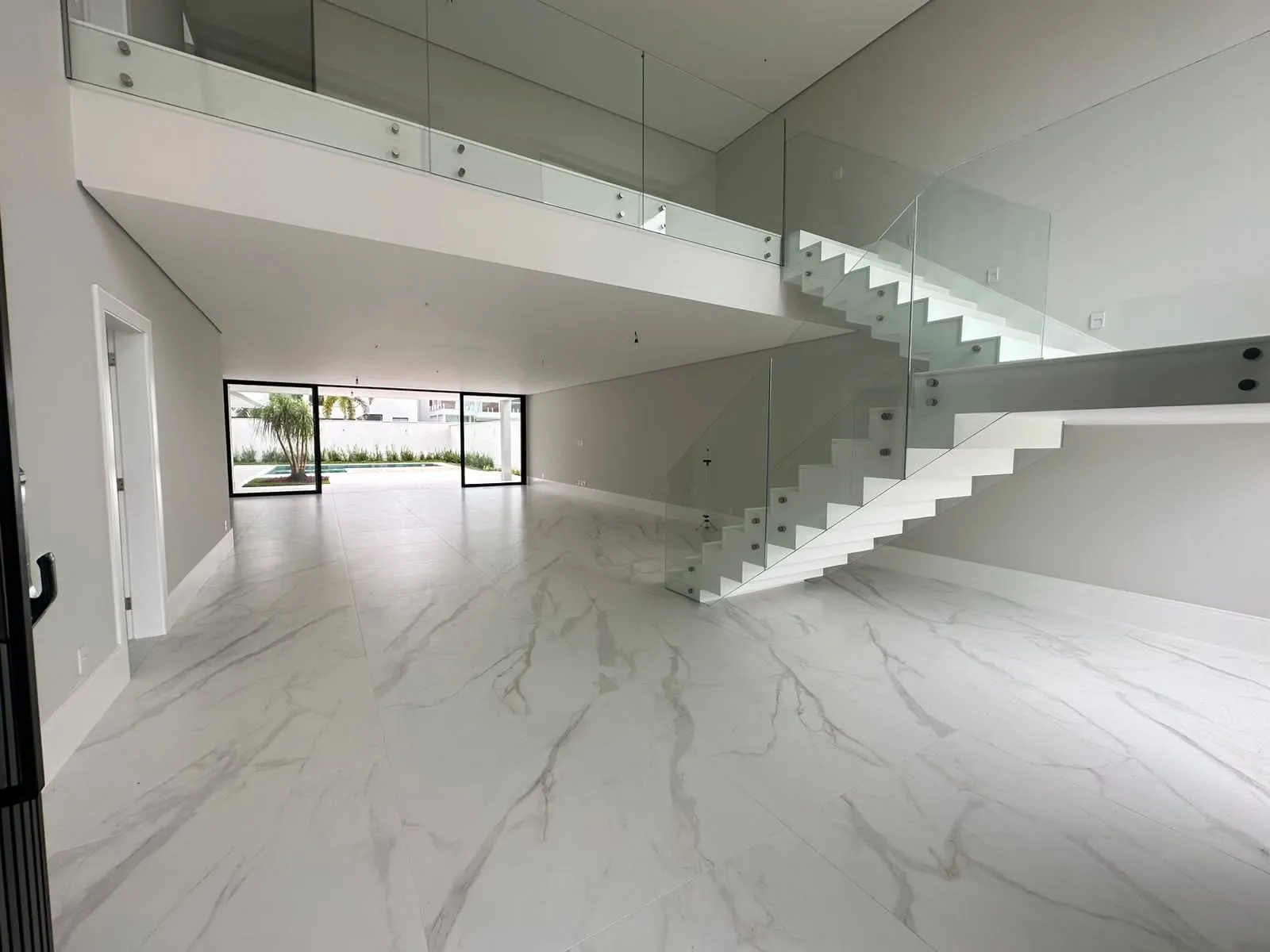 Sala ampla com pé direito duplo, piso de mármore e escada com guarda-corpo de vidro