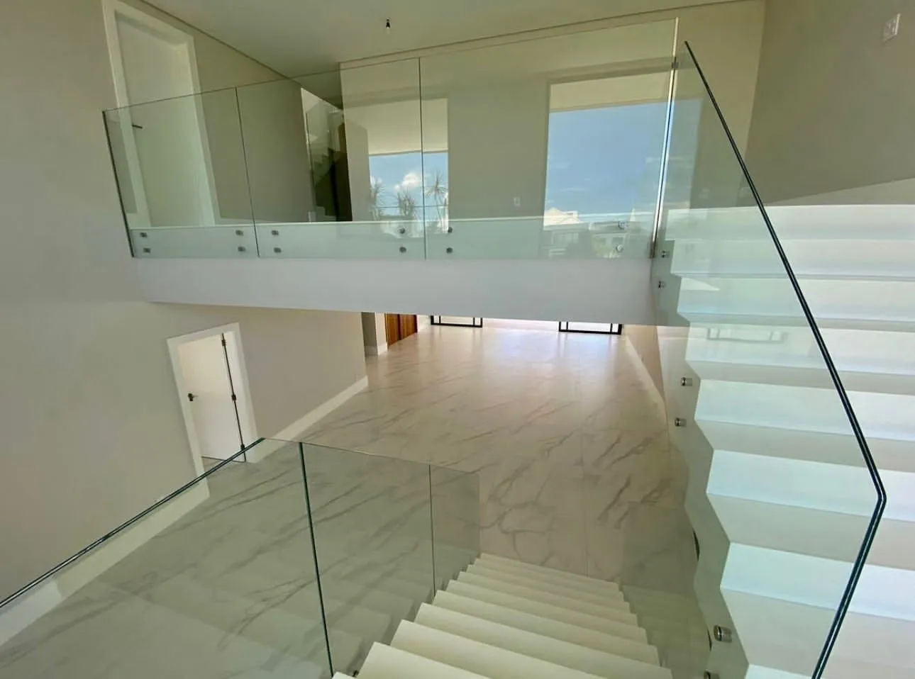 Escada em mármore branco com guarda-corpo de vidro e estrutura metálica