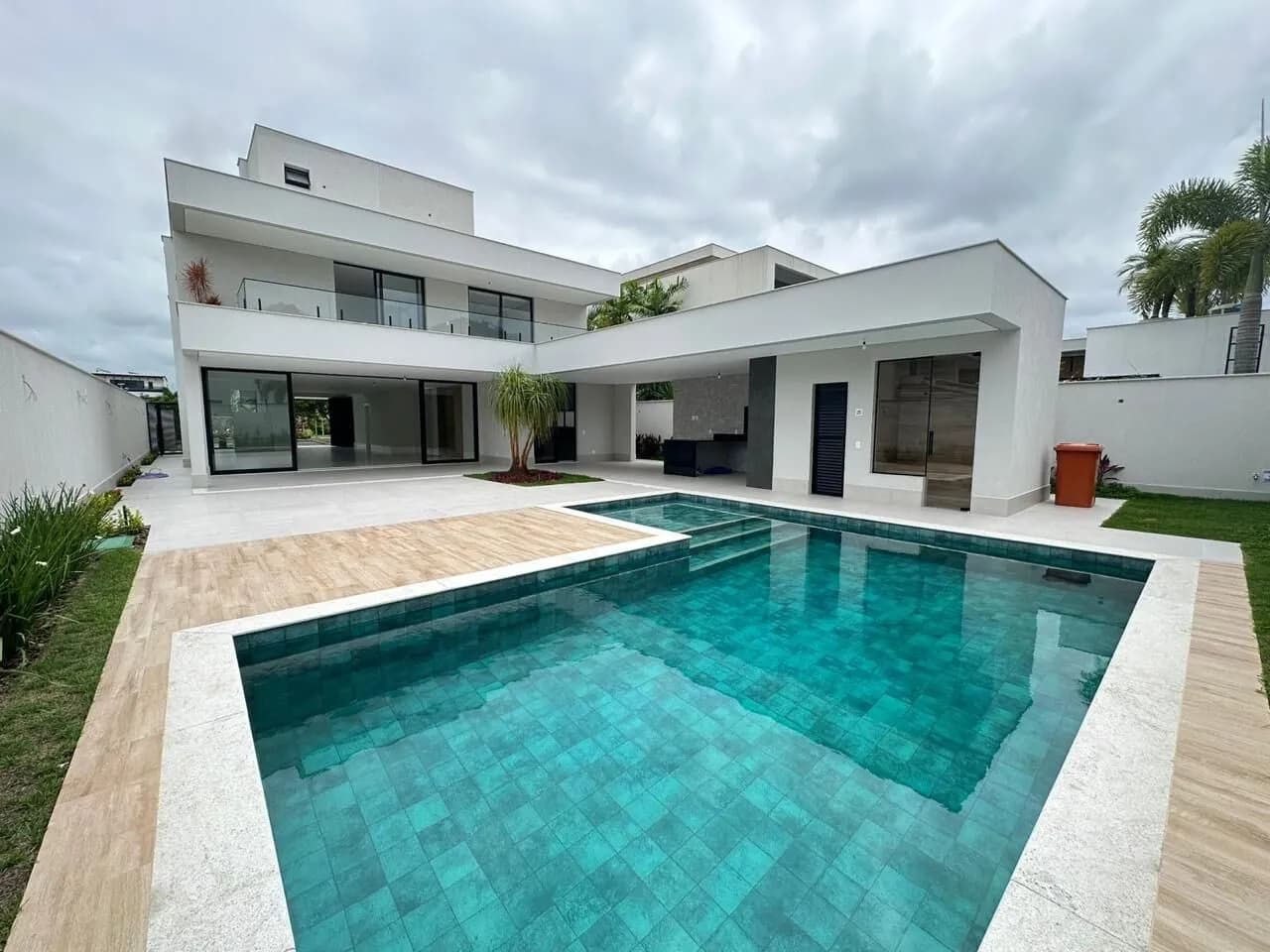 Vista da fachada posterior e piscina com deck de madeira da casa duplex no Alphaville Barra da Tijuca