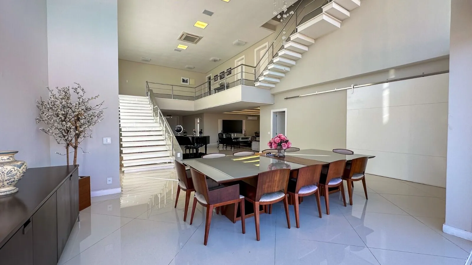 Sala de jantar com pé-direito duplo, escada escultural e mesa para 10 lugares na Casa Alphaville 800m²